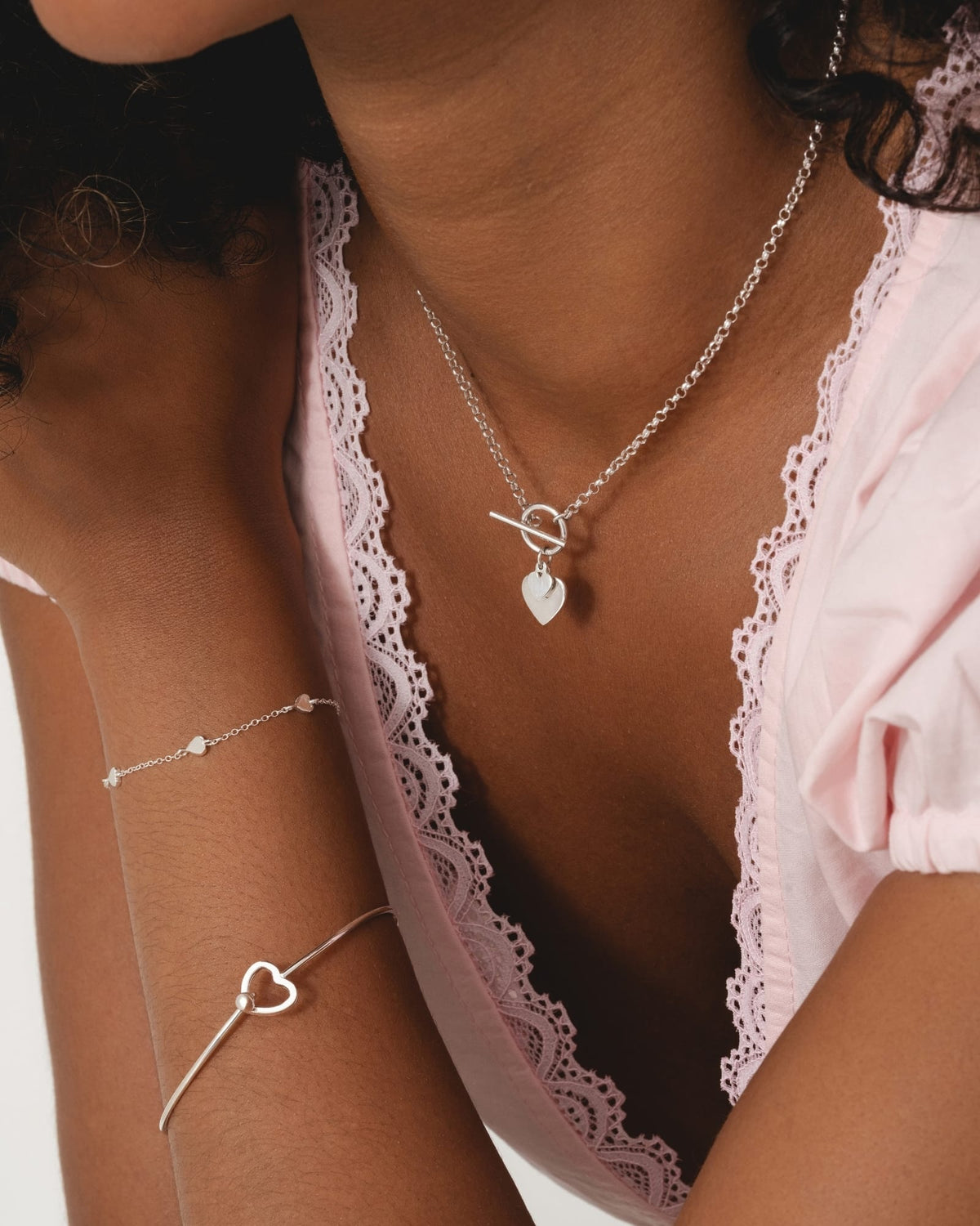 Delicate sterling silver bracelet featuring three mini heart charms worn on a wrist alongside a matching silver heart bangle.