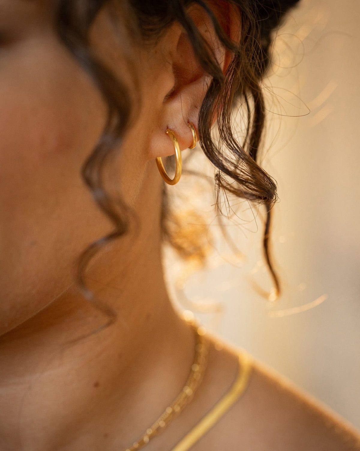Small 10mm gold-plated sterling silver hoop earrings worn in first and second ear piercings.