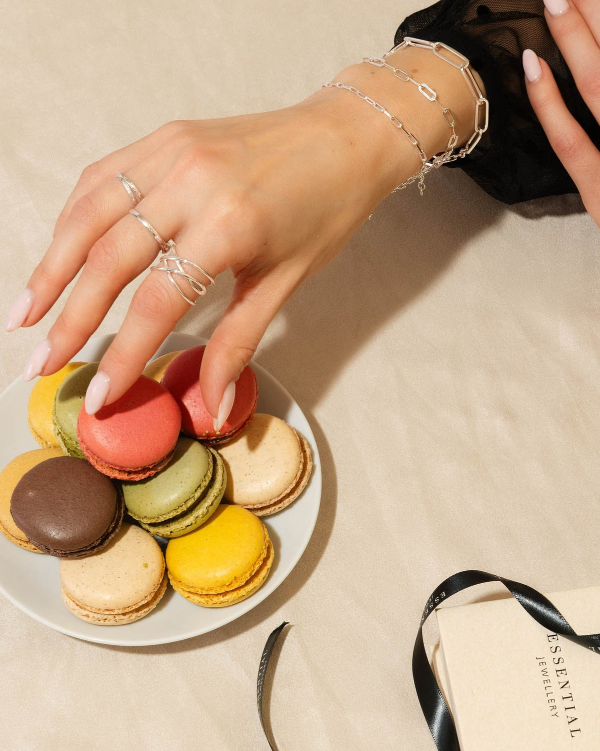 Polished 1.5mm sterling silver flat band ring worn stacked on a hand reaching for colorful macarons.