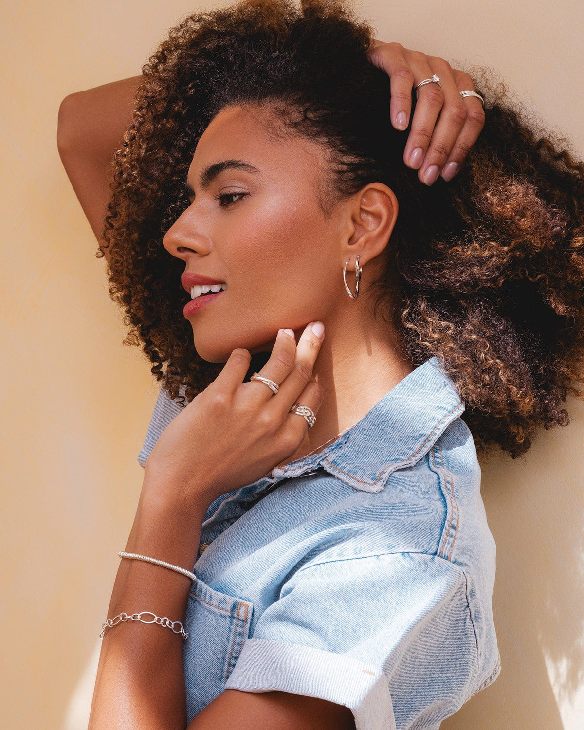 Woman wearing a polished sterling silver sweetie slider bracelet on her wrist with matching silver rings and hoop earrings.
