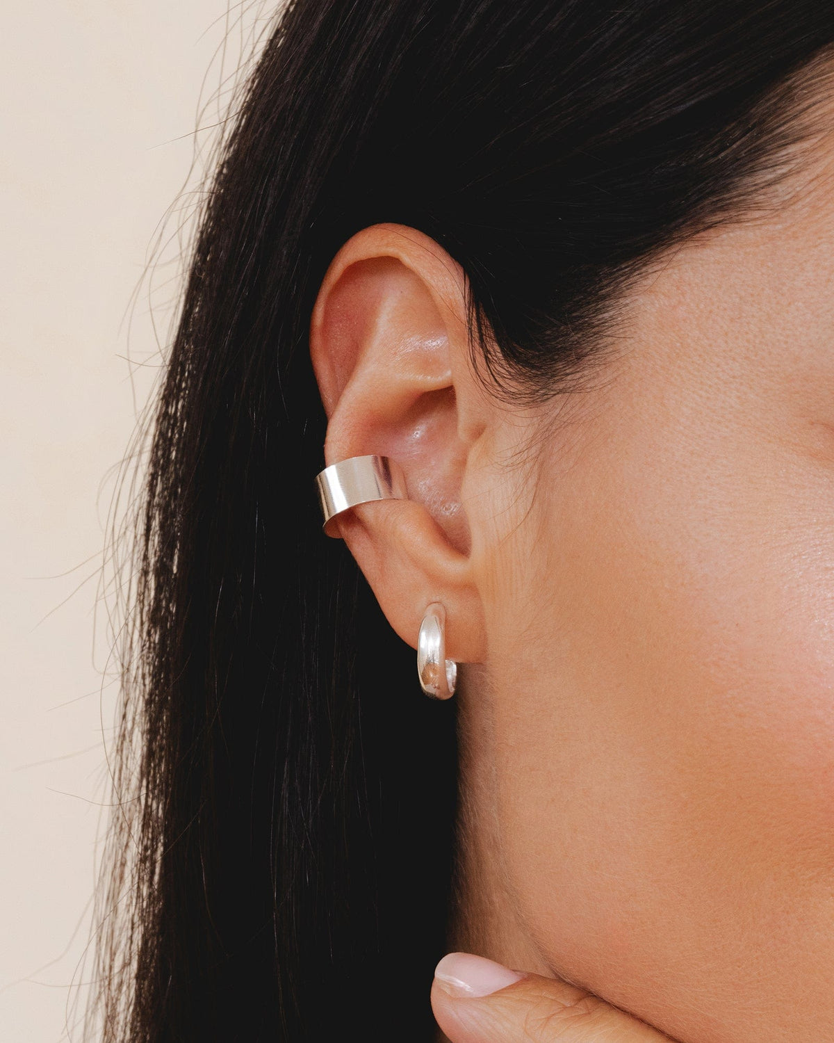 Small, polished sterling silver hoop earring worn on an earlobe next to a wide silver ear cuff.