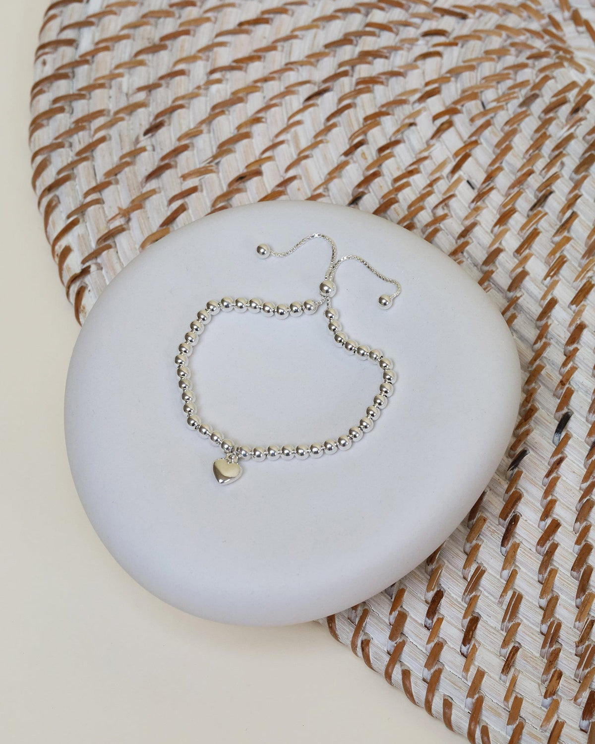 Sterling silver beaded slider bracelet on a box chain with a puffed heart charm resting on a white stone.