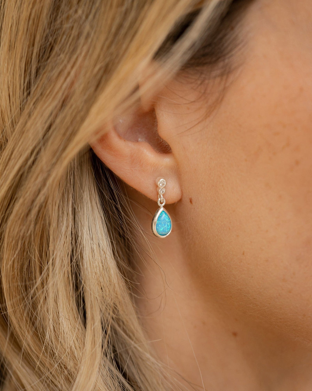 Sterling silver teardrop earrings featuring a vibrant blue opal and sparkling cubic zirconia studs worn on an ear.