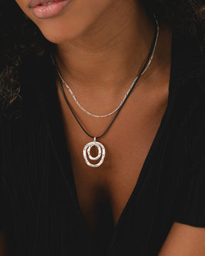 Sterling silver light Figaro chain layered with a black cord necklace featuring two interlocking silver rings.