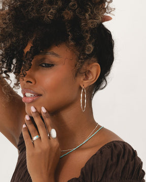 Large sterling silver hoop earrings with a delicate twisted design worn by a woman with curly hair.