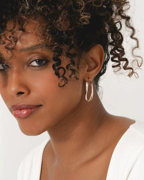 Model wearing polished sterling silver chunky hoop earrings with an organic, twisted O-shape design.