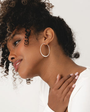 Model wearing sleek, polished sterling silver creole hoop earrings with a minimalist, modern design.
