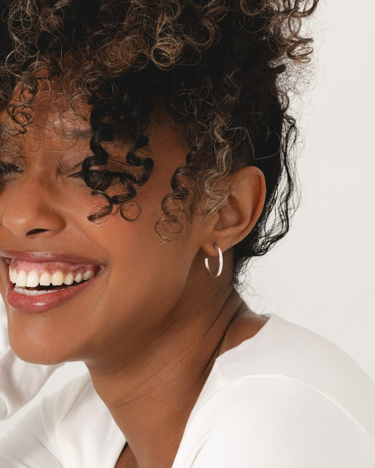 A woman wearing 20mm square tube hoop earrings crafted from polished sterling silver.