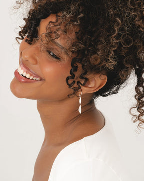 Smiling woman wearing polished sterling silver drop earrings with a sculptural, tapered twist design on hook fittings.