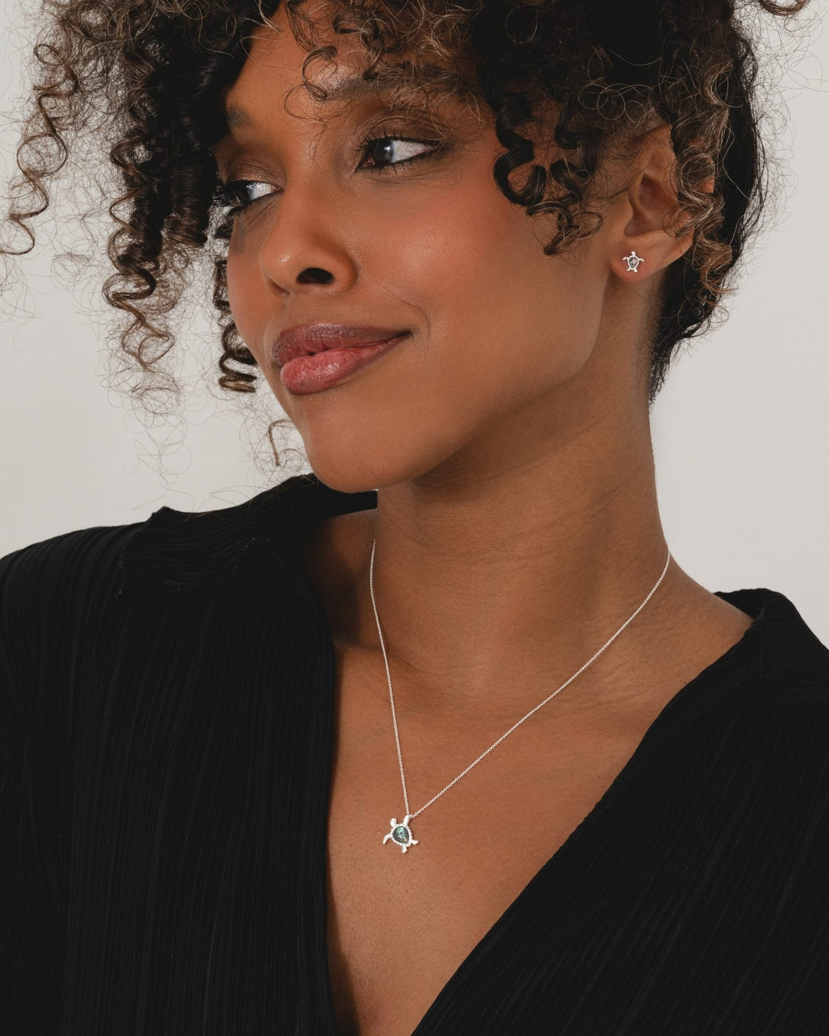 Sterling silver turtle necklace with iridescent paua shell inlay worn by a woman with matching turtle stud earrings.