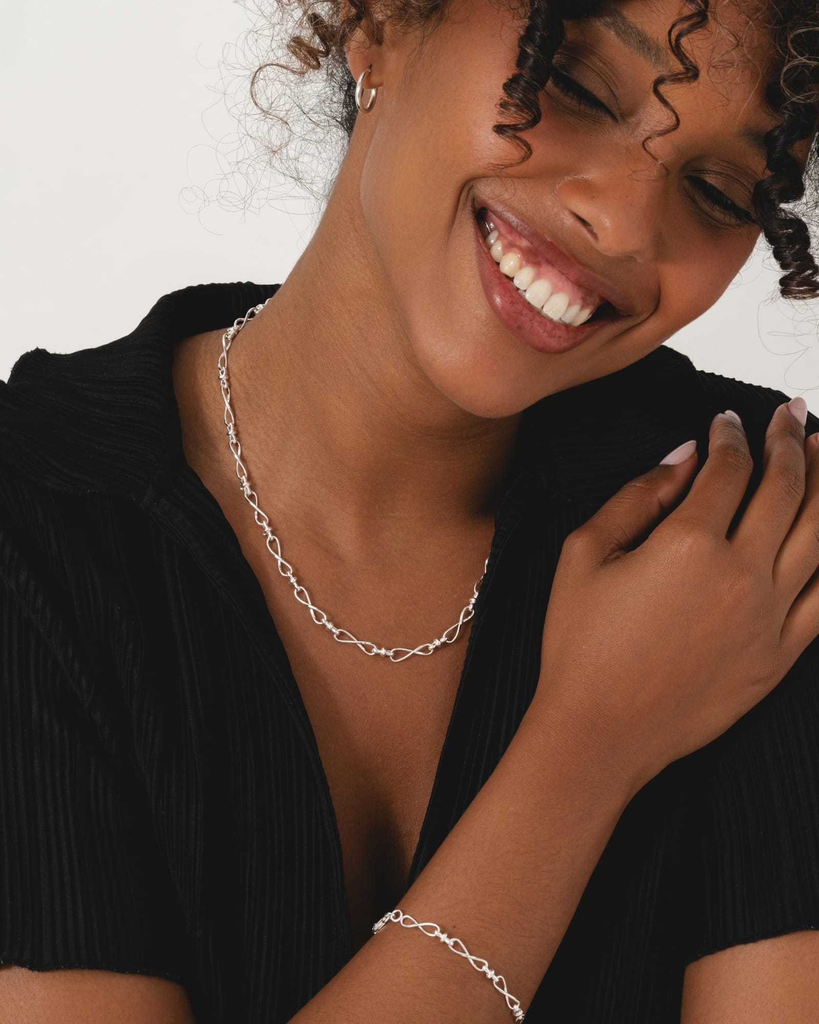 18-inch sterling silver infinity link necklace worn by a smiling woman in a black top.