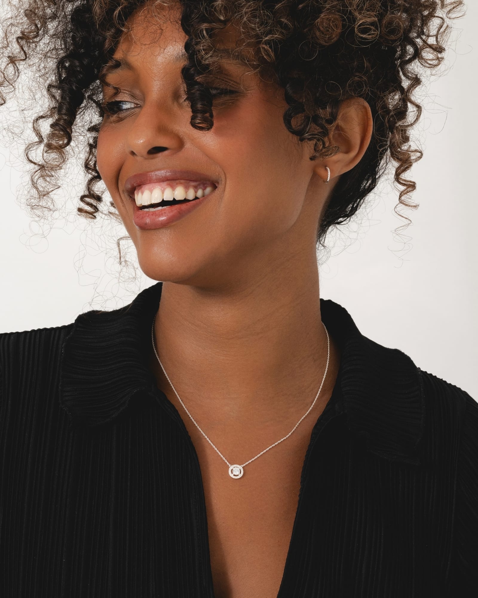 Sterling silver halo necklace with a central cubic zirconia stone on a fine chain worn by a smiling woman.