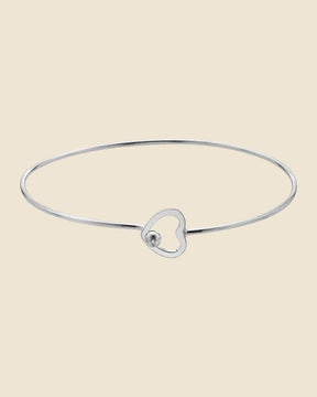 Minimalist sterling silver bangle featuring a delicate heart-shaped clasp on a thin, polished metal band.