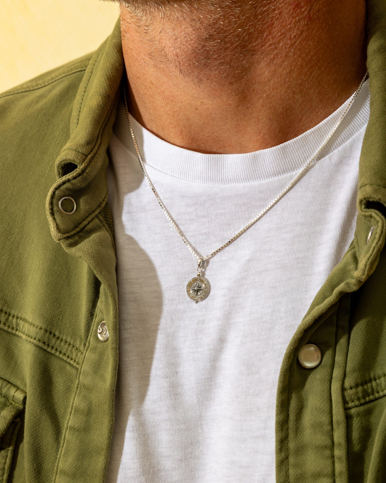 Oxidised sterling silver compass pendant on a delicate silver chain worn around a man's neck.