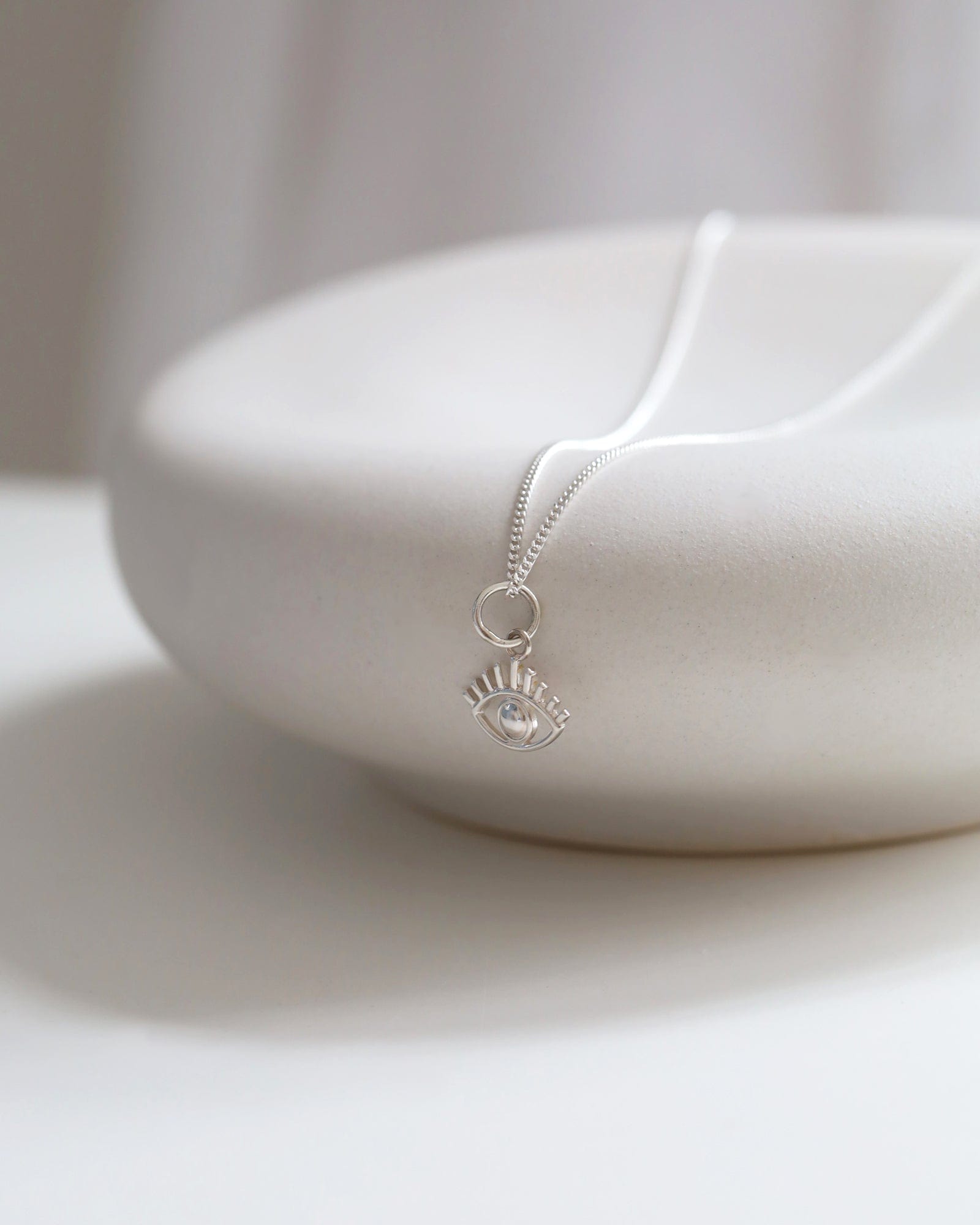 Dainty sterling silver evil eye pendant on a delicate chain resting on a smooth white stone surface.