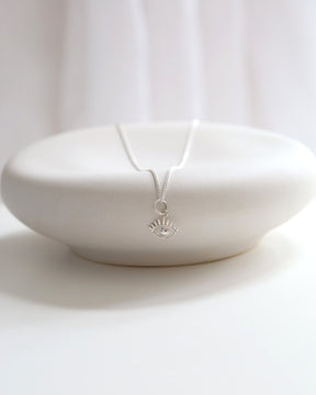 Dainty sterling silver evil eye pendant on a delicate chain, resting on a minimalist white ceramic dish.