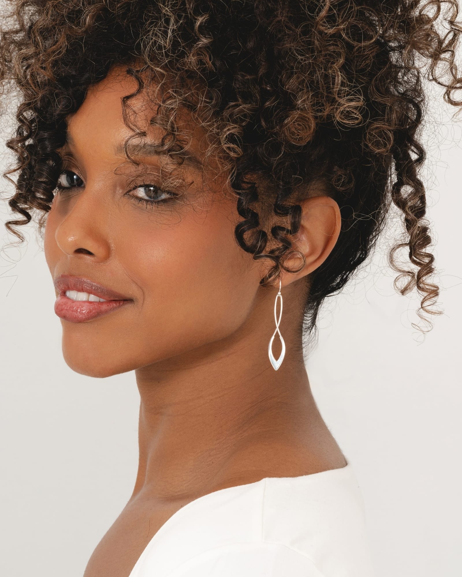 Polished sterling silver wishbone drop earrings worn by a woman with curly hair.